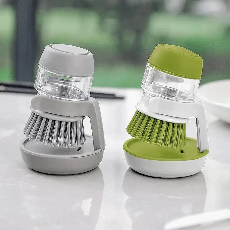 Two kitchen cleaning brushes, one gray and one green, on a reflective surface with a blurred outdoor background.